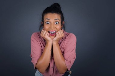 Esmer kadının stüdyodaki görüntüleri ellerini çenesinin altında tutuyor, keyifli bir ruh hali içinde, ertesi gün için arkadaş fikrini seviyor. Gri duvarda tek başına..