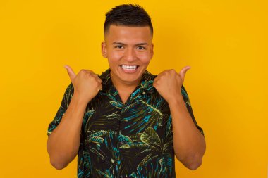 Arka planda izole edilmiş, olumlu içerik ve mutluluk duygularıyla baş parmaklarını gösteren iyimser, genç bir İspanyol erkek. Ortak alan, kalite ve tavsiye ile tatmin kavramı.