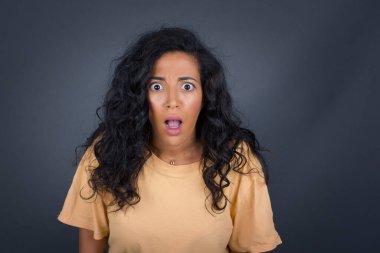 Çekici genç esmer kadın, ağzı açık ve çenesi düşmüş, sersemlemiş ve şok olmuş bakışlar içinde.