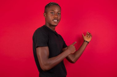 Olumlu ifadeli, hoş, Afro-Amerikalı bir adam, gelişigüzel giyinmiş, promosyon metnin ya da ilanın için boş fotokopi alanına işaret ediyor. Sevimli adam evde tek başına poz veriyor.