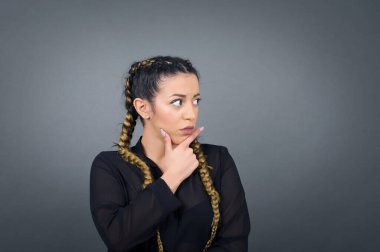 Tarz sahibi, genç esmer kadın portresi. Çenesinin altında elleri var ve yana bakıyor. Şüpheli ve şüpheci bir ifadeyle, endişe ve şüpheyle. Gri arka planda kapalı duruyor..