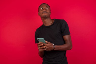 Kırmızı arka plan üzerinde siyah tişört giyen mutlu bir Afro-Amerikalı adamın resmi cep telefonu kullanıyor..