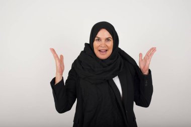 Başarı, başarı konsepti. Siyah tesettürlü neşeli Müslüman kadın ellerini kaldırıyor, mutluluk dolu gözleriyle büyük başarılarını kutluyor..