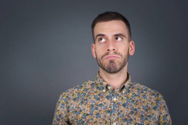 Kafası karışık, beyaz bir adam yüzünü buruşturur, dudaklarını ısırır, kaşlarını kaldırır, yukarı bakar, sorunları olur, şık kıyafetler giyer, gri arka planda soyutlanır, pişman olur..