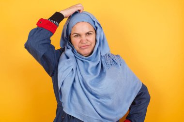 Tüh, ne yaptım ben? Orta yaşlı, tesettürlü, korkmuş ve pişmanlık dolu bir ifadeyle el ele tutuşan güzel Müslüman kadın. Arka planda dikilen günlük kıyafetlerle..