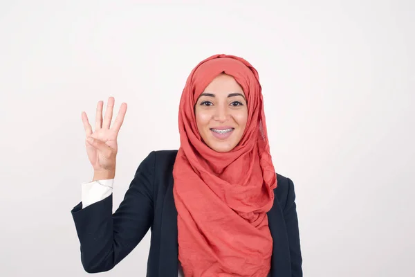 美しいイスラム教徒の女性は 灰色の壁に立って黒いブレザーとヒジャブを着用し 自信と幸せに微笑んでいる間 指番号4を指で指で指を指さす — ストック写真