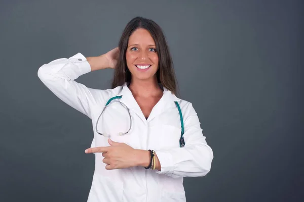 Vreugdevolle Jonge Doktersvrouw Geïsoleerd Grijze Achtergrond Medisch Uniform Demonstreert Iets — Stockfoto
