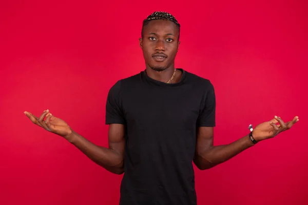 Portrait of African American man wearing black t-shirt over red background looks uncertain. Man dressed up to go to the bar with girl he met in social network but she did not show up. Why she did not come? Question bothers our hopeless romantic.