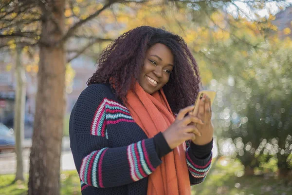 Όμορφη Αφροαμερικανή Γυναίκα Μακριά Μαλλιά Φορώντας Πολύχρωμο Πουλόβερ Κρατώντας Smartphone — Φωτογραφία Αρχείου