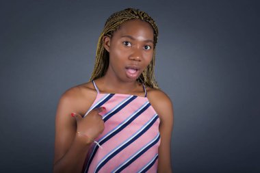 Şaşırmış güzel, şaşkın bir ifadeye sahip ve kendini parmağıyla işaret ediyor. Gri arkaplan üzerinde izole.