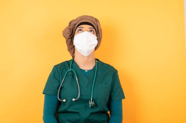 Yeşil tıp üniformalı, esrarengiz bir gülümsemeyle yukarı bakan güzel Müslüman kadın portresi. Güzel, gülümseyen kız duvara bakıyor..