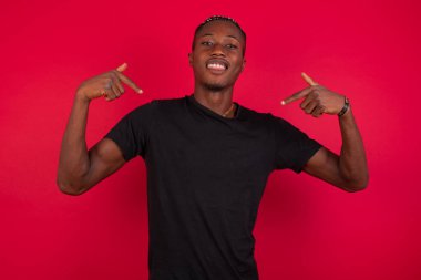 Kırmızı arka planda siyah tişört giyen doğru Afrikalı Amerikalıyı buldun, beni seç! Kendine güvenen, kendine güvenen ve karizmatik bir oyuncu. Moda elbisesi içinde kendini tanıtıyor. Geniş bir gülümseme istiyor ve vücuduna işaret ediyor.