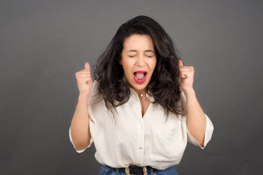 Güzel esmer kadın yumruklarıyla sıradan giyinmiş. Gri arkaplanda duruyor.  