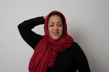 Tüh, ne yaptım ben? Olgun Müslüman kadın korkmuş ve pişmanlık dolu bir ifadeyle el ele tutuşuyor. Gri arka planda dikilen günlük kıyafetlerle. Stüdyoda poz veren başörtüsü takan orta yaşlı bir Arap kadın.