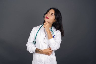 Düşünceli gülümseyen bir doktorun portresi elini çenesinin altında tutar, yan bakar, ilgi çekici bir şey düşünür, gri stüdyoya karşı poz verir. Karar alma kavramı.