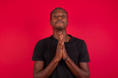 Afro-Amerikan bir adamın yatay portresi avuç içlerini bir arada tutuyor ve mutlu bir ifade takınıyor. Çekici bir erkek merhamet diliyor. Umutlu genç yetişkin.