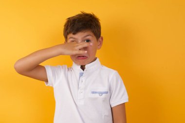 Şirin çocuk sarı duvara karşı burnunu kapatıyor.  