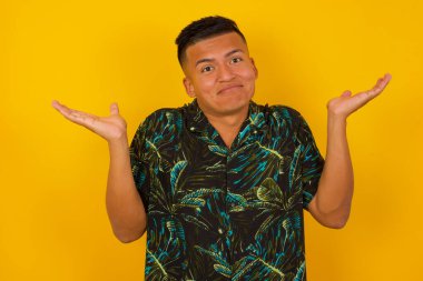 İfadesi şüphe dolu yakışıklı bir adam, şaşırmış ve şaşırmış, belirsiz gelecek omuzlarını silkiyor, sarı duvara karşı duruyor..