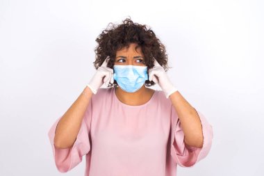 Yüz maskesi takan ve beyaz stüdyo arka planında izole edilmiş günlük kıyafetler giyen bir kadın.