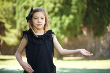 Siyah elbiseli güzel bir kızın portresi. Parkta hoş geldin jesti yapıyor. 