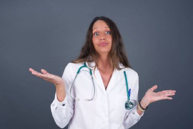 Güzel doktor kadın ifadeden şüphe ediyor, şaşırıyor ve merak ediyor, belirsiz bir gelecek omuz silkiyor, gri duvara karşı duruyor..