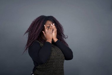 Endişe - güzel bir Afro-Amerikan kadınının kavramsal görüntüsü. Günlük giysiler içinde yüzünü elleriyle kapatıyor ve bir gözü kapalı içeride dikiliyor. Bir şeyden ya da birinden korktun mu?.