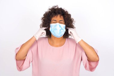 Yüz maskesi takan ve kulaklarını kapatan kadın beyaz stüdyo arka planında izole edilmiş.
