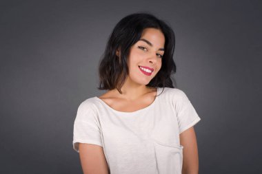 Utangaç kız kameraya bakarak gülümsüyor. Beyaz tenli çekici kız gri stüdyo geçmişine karşı zımparalıyor. Utangaç..