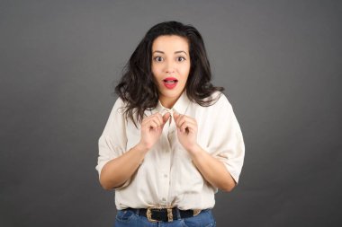 Güzel esmer kadın şaşırdı. Gri arkaplanda duruyor.