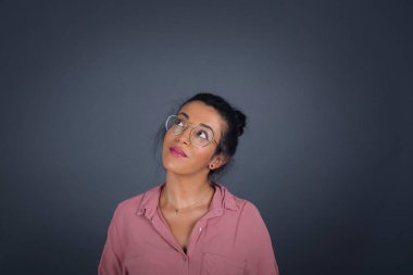 Gizemli esmer kadın portresi. Gözlüklü, gri duvara bakarken yukarı bakıyor.. 