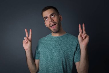 Neşeli Avrupalı bir adamın yalnız çekimi iki eliyle barış ya da zafer işareti yapar, rahat kıyafetler giyer, serin hisseder dişli bir gülümsemesi vardır, gri arka planda izole olur. İnsanlar ve vücut dili.