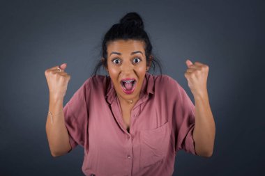 Güçlü, başarılı, kararlı, pembe gömlekli, kollarını kaldıran, yumruklarını sıkan, neşe ve heyecanla bağıran genç bir kadının portresi..