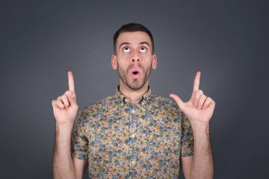 Yakışıklı, zarif bir adamın portresi izole edilmiş arka planda şaşkın şaşkın bakıyor ve parmaklarıyla garip bir şey gösteriyor..