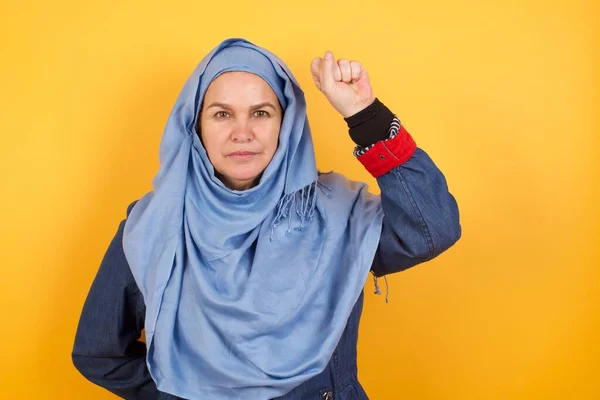 ヒジャーブにいる中年のイスラム教徒の女性は 真剣で強く反抗的で イエローウォールに対する革命のために拳を上げたり 抗議したり 戦ったりしています — ストック写真