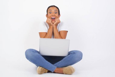 Diz üstü bilgisayarı olan mutlu Arap kadının stüdyo fotoğrafları, çenesinin altında el ele tutuşur, keyifli bir ruh halinde olur, ertesi gün için arkadaş fikrini sever, duvarda izole olur. Pozitif duygular.