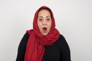 Etkileyici yüz ifadeleri. Şok olmuş kadın, çenesi düşük, boş gri duvarda gördüklerinden sersemlemiş hissediyor. Stüdyoda poz veren başörtüsü takan orta yaşlı bir Arap kadın.