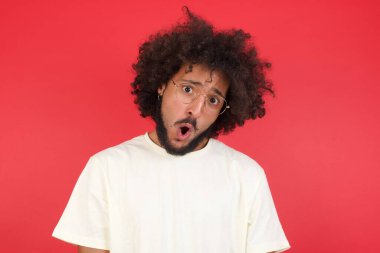 Afro saçlı genç adamın kırmızı duvara karşı kafası karışık. 
