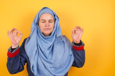 Meditasyon, din ve ruhani uygulamalar. Güzel, orta yaşlı, tesettürlü Müslüman kadın gözlerini kapalı tutuyor, parmaklarını Mudra hareketinde tutuyor..