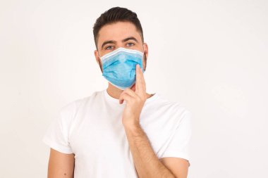 Medikal maske takan başarılı beyaz adam ders verirken kendine güvenen, kendine güvenen, çene hattına dokunarak gülümseyen, başını eğen, beyaz dişlerini sallayan bir iş adamı nasıl olur da mutlu olur?