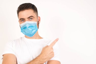 Tıbbi maske takan heyecanlı adam, moda reklamcılığı ve tanıtım metinleriniz için gri arka plan fotokopisi çekerken mutlu bir şekilde kenara çekiliyor..