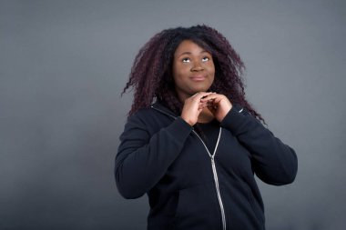 Sıradan giysiler içinde, stüdyoda aylak aylak dolaşıp zıplayan Afro-Amerikan kadını oldukça şaşırttı. Sevimli kız renkli arka planda dans ediyor ve elleriyle çeneye dokunuyor.