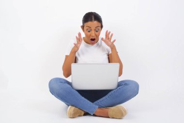 Işık arkaplanına dayanmış genç bir kadının portresi, şok olmuş yüz ifadesiyle yüz yüze, çığlık atarak ve yan gözle hayret verici bir şeye bakarken. Dizüstü bilgisayar kullanan güzel bir Arap kadın.