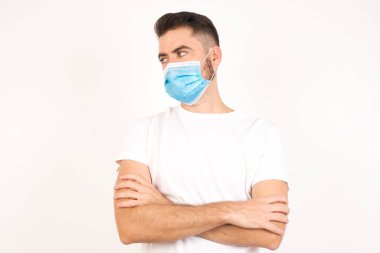 Closeup portrait displeased pissed off angry grumpy pessimistic man with bad attitude, arms crossed looking sideways. Negative human emotion facial expression feelings. Caucasian man wearing medical mask 