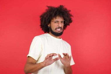 Afro saçlı genç adam kırmızı duvardan iğreniyor.   