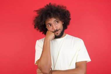 Kızıl duvara karşı düşünen afro saçlı genç bir adam.   