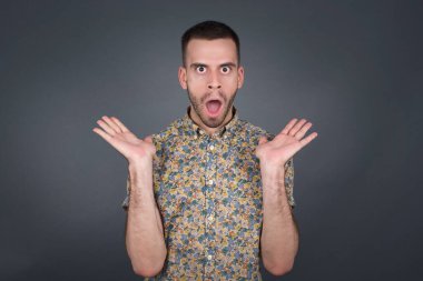 Şaşırmış genç bir adamın portresi. İnanamamasına şaşırmış gibi görünüyor. Ağzın açık ve yüzün yanında elleri var. Olumlu duygu yüz ifadesi vücut dili.