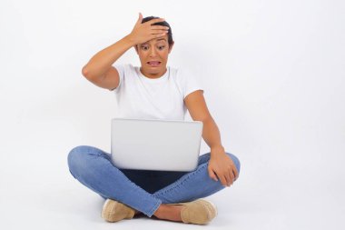 Tüh, ne yaptım ben? Güzel bir kadın, korkmuş ve pişmanlık dolu bir ifadeyle elini alnından tutuyor. Günlük giysiler giyiyordu. Genç Arap kadın dizüstü bilgisayar kullanıyor.