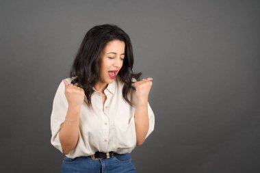 Güzel esmer kadın bağırıyor. Gri arkaplanda duruyor. 