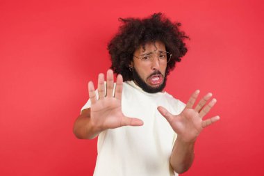 Afro saçlı genç adam kırmızı duvarda durdu.   