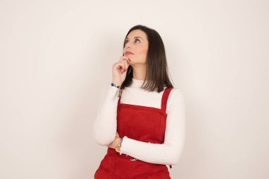 Düşünceli gülümseyen kızın portresi elini çenesinin altında tutuyor, yan bakıyor, ilgi çekici bir şey düşünüyor ya da merak ediyor, sıradan giyiniyor, gri stüdyoya karşı poz veriyor. Karar alma kavramı.